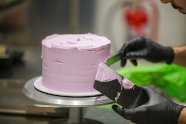 Pasta şefi spatula ve kazıyıcı kullanarak pürüzsüz katmanlı leylak kremalı pasta - düğün pastası hazırlığı