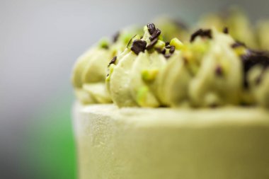 Pasta tasarımcısı yeşil katmanlı çikolatalı kekin üzerine küçük pistacchio ve koyu çikolata parçaları serpiyor.