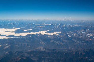 Mavi gökyüzünün altındaki dağların ve vadilerin havadan görünüşü.