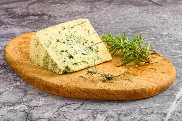 Tahta üzerinde otlar olan bir parça peynir.