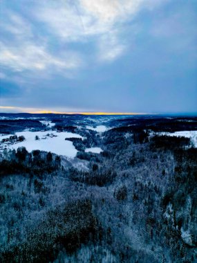 Akşam karanlığında bulutlu gökyüzünün altında karlı bir manzara.