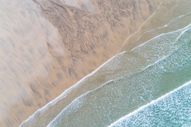 Kumsalın insansız hava aracının yukarıdan görünüşü. Dalgalar ıslak kumun üzerinde alçak gelgitte süzülüyor.