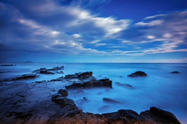 Kayalık kıyı şeridi ile okyanus manzarası ve bulutlarla dolu dramatik mavi gökyüzü