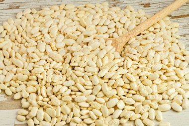 Bir avuç beyaz fasulye ve ortada bir tahta kaşık.