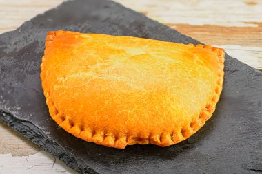 Golden baked empanada on slate