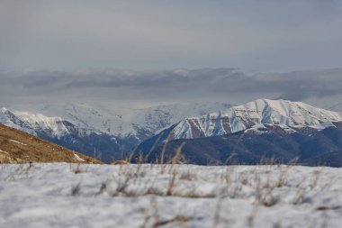 Kışın bulutlu bir gökyüzünün altında karla kaplı dağlar..