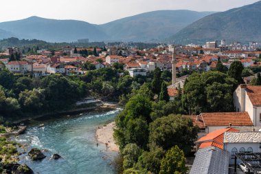 A picturesque scene of Neretva River peacefully flowing amidst a vibrant green hillside in Mostar, Bosnia and Herzegovina