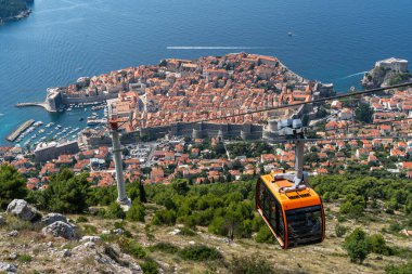 A cable car steadily climbs a hill, transporting passengers while the city of Dubrovnik provides a stunning backdrop, Croatia