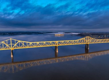 Sarı köprü bulutların altında sakin bir nehri kaplıyor.