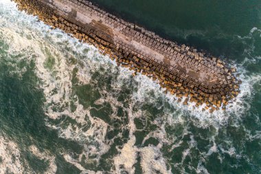 Dalgakıranın ve gün batımında dalgaların köpüğünün drone üst görüntüsü