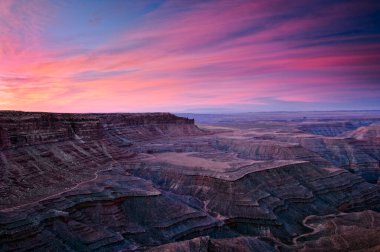 Muley Point 'teki geniş bir kanyon göz kamaştırıcı pembe, mor ve mavi günbatımı gökyüzü ile aydınlanır..