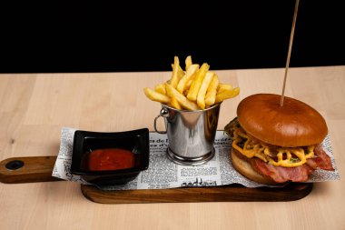 Hamburger, peynir ve patates kızartmasının metal kapta servis edildiği yakın çekim görüntüsü.