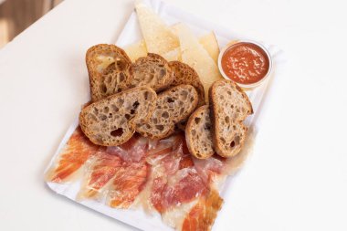 Dilimlenmiş ekmek, peynir, İspanyol sucuğu ve sos tabağı.