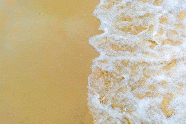 Waves crashing onto sandy beach creating foamy white texture