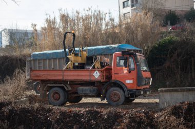 Turuncu bir Mercedes Benz 1414 inşaat kamyonunun yan görüntüsü sarı bir Caterpillar CB-214 yol silindiri yüklüyor..
