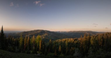 Alacakaranlıkta açık mavi gökyüzünün altındaki yemyeşil tepelerin panoramik manzarası