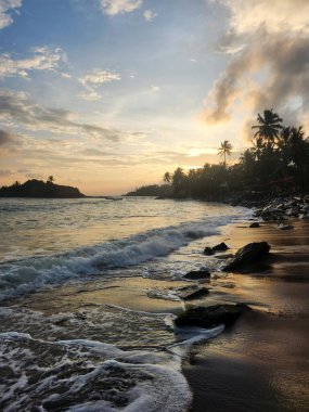 Gün batımında dalgalar kayalık sahile çarpıyor.