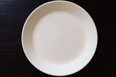 Empty white plate on black wooden table. top view