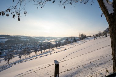 Tepeler ve ağaçlarla kaplı karlı bir manzara.