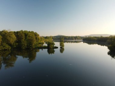 Bereketli ağaçlarla çevrili sakin bir göl manzarası.