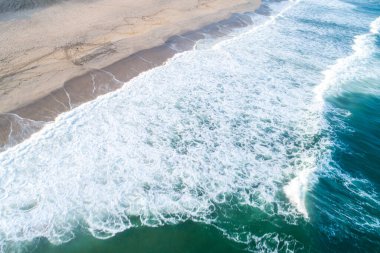 Kumsalın hava aracı görüntüsü. Kumlu deniz kıyısı, yeşil dalgalar ve beyaz köpüklü yaz arkaplanı..   