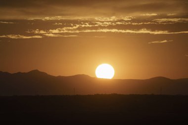 Güneş renkli gökyüzü ile dağların üzerinde batıyor.