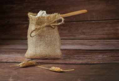 Tahta bir kaşık içinde un ve tahtadan bir masa ve buğday kulaklı çuval.