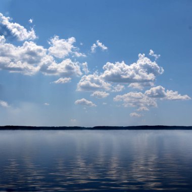 Sakin su bulutları ve mavi gökyüzünü yansıtıyor.