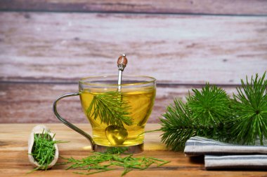 At kuyruğundan yeni demlenmiş, ahşap bir masada cam bir fincanda servis edilen tıbbi bir bitki çayı.