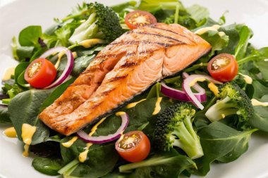 Taze yeşil salata ile servis edilen ızgara somon filetosu.