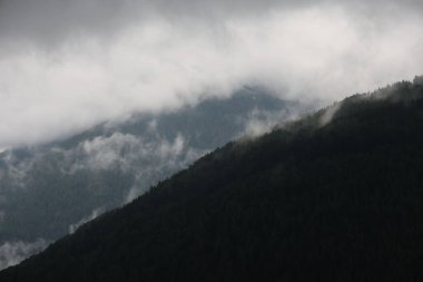 Kara bulutlu gökyüzünün altında dramatik dağ manzarası.