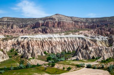 Mavi gökyüzünün altında kaya oluşumlarının yer aldığı manzaralı bir yer..
