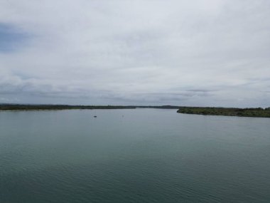 Geniş nehir manzarası bulutlu gökyüzü altında yeşillik.