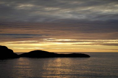 Uzak kayalık adalarla sakin okyanusun üzerinde gün batımı