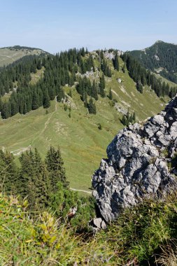 Geniş dağ manzarasını, engebeli kaya oluşumunu, yeşil yamaçları, mavi gökyüzünü gözlemliyorum..