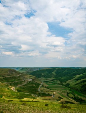 Bulutlu gökyüzünün altında yuvarlanan yeşil tepeler