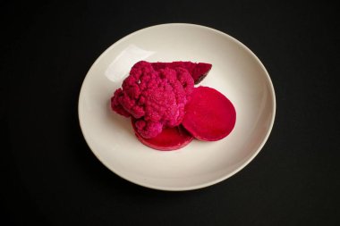 Siyah arka planda beyaz tabaktaki canlı pembe yiyeceklerden oluşan yaratıcı bir yemek.