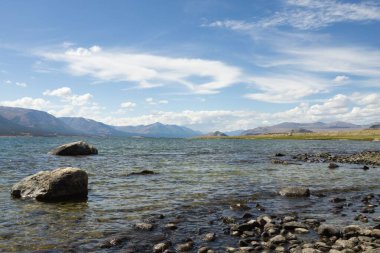 Açık mavi göl Parlak gökyüzünün altındaki uzak dağlarla çevrili