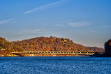 Arka planda sonbahar yeşillik tepeleri ve sakin mavi suya yayılan köprü manzarası