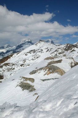 Karla kaplı dağ manzarası mavi gökyüzünün altında dağınık bulutlarla