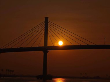 Silüet kabloyla suyla örülmüş köprünün arkasında güneş batıyor.