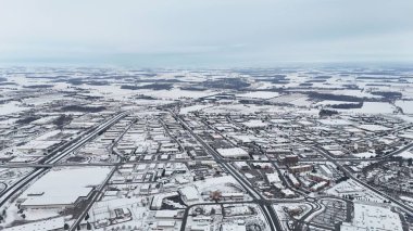Karla kaplı şehir manzarasını yollar, binalar ve ağaçlarla gösteren hava manzarası.