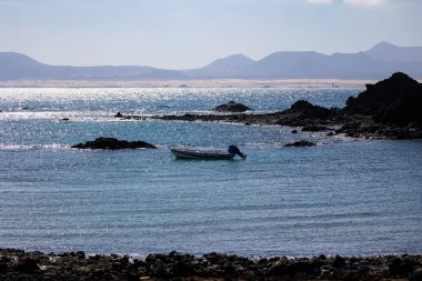 Kayalık kıyılarda sakin sularda yüzen küçük bir tekne.