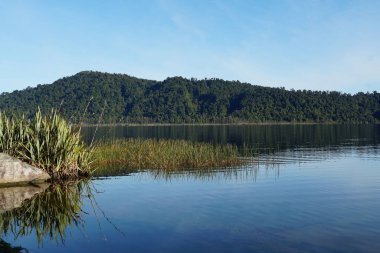 Sakin göl yeşil tepeleri ve bitkileri yansıtıyor.
