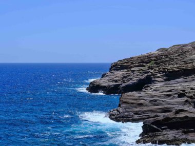 Dalgaların kayalık yüzeye çarptığı dalgalı mavi okyanusa bakan kayalıklar