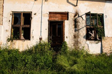 Eski terk edilmiş bir ev, camları kırık, etrafı çimlerle çevrili.