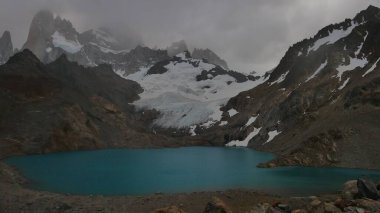 Engebeli dağlar ve buzullarla çevrili turkuaz bir göl.