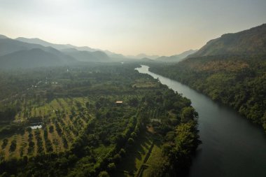 Dağlarla çevrili yeşil arazide akan kıvrımlı nehrin havadan görünüşü