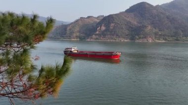 Kırmızı Kargo Mavnası Yeşil Dağlar 'ın yanındaki Geniş Nehir' de ilerliyor.