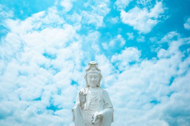 Beyaz Budist tanrı heykeli açık havada, mavi bulutlu gökyüzünün altında duruyor..